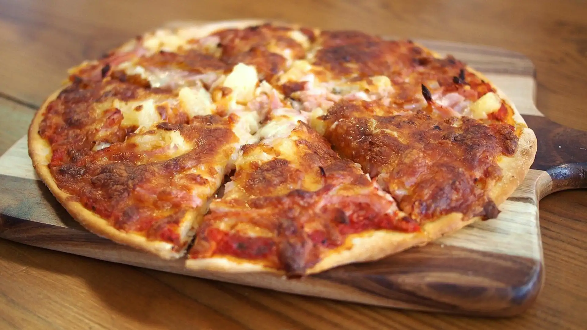 Nous pouvons voir une pizza margherita posée sur une planche de présentation, elle même sur une table en bois